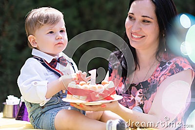 delightful baby boy, accompanied by his mother, birthday celebration cake with 1 candle. Stock Photo
