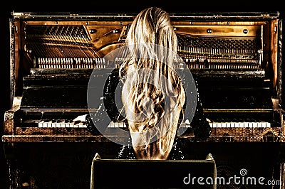 Delightful girl with luxurious long hair plays a retro piano. Back view Stock Photo