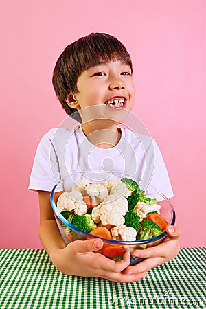 Delightful mealtime. Smiling boy, child sitting at table with bowl full of boiled broccoli, carrots, and cauliflower Stock Photo