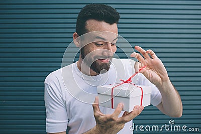 Delightful and nice guy is opening the present box. He is looking at irt and pulling out red ribbon. He is very excited Stock Photo