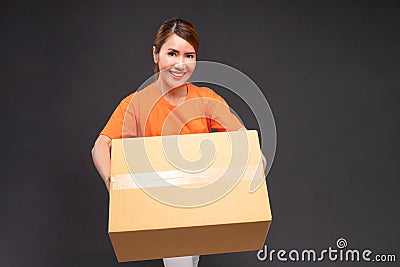 Delivery asian woman or courier wearing an orange uniform holds a cardboard box in studio Stock Photo