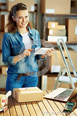 Smiling modern woman in jeans using tablet PC app in warehouse Stock Photo