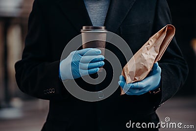Delivery service during coronavirus and quarantine. Faceless businessman holds take away food and disposable cup of coffee, wears Stock Photo