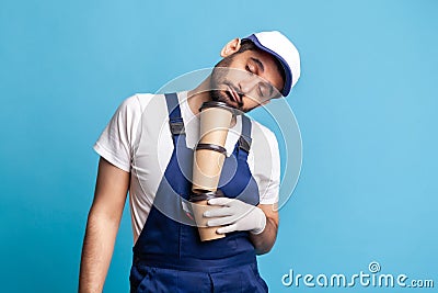 Delivery service. Tired inefficient courier man in overalls lying on coffee cups and sleeping, feeling exhausted Stock Photo