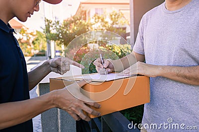 Delivery young man standing at the door of home and carrying parcels for young male to signing Stock Photo