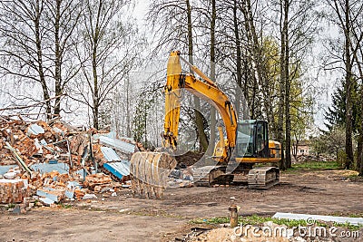 Demolition of an old house with an excavator. Cleaning up a destroyed house with an excavator after the bombing. Stock Photo