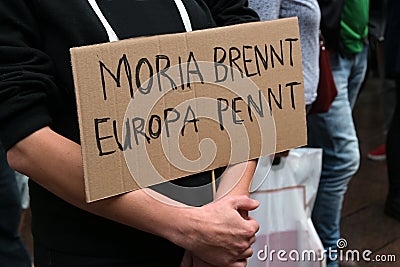 Demonstrator holds a cardboard sign with German text Moria brennt, Europa pennt, meaning Moria is burning, Europe is sleeping, on Stock Photo