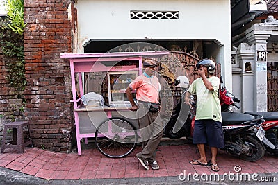 DENPASAR/BALI-APRIL 20 2019: a street meatball seller uses a pink cart and wears a pink shirt chatting with his buyers on the Editorial Stock Photo