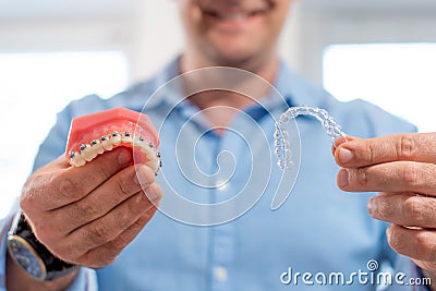 Dental care.Smiling dentist doctor holding aligners and braces in hand shows the difference between them Stock Photo