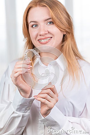 Dental care.Smiling girl with braces on her teeth holds aligners in her hands and shows the difference between them Stock Photo