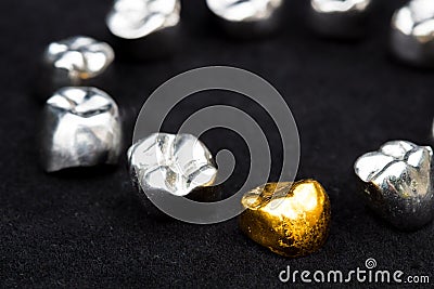 Dental gold and metal tooth crowns on dark black surface. Stock Photo
