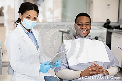 Dental Insurance Concept. Black Dentist Woman And Male Patient Posing In Clinic Stock Photo