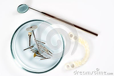 Dental medical tools, dentist equipment: stomatological mirror, false white teeth and used dental burs in Petri dish glass on Stock Photo