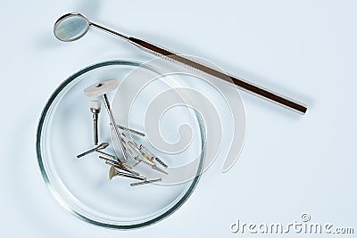 Dental medical tools, dentist equipment: stomatological mirror and used dental burs in Petri dish glass on light blue Stock Photo