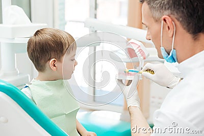 Dentist educating little boy about brushing teeth in clinic Stock Photo