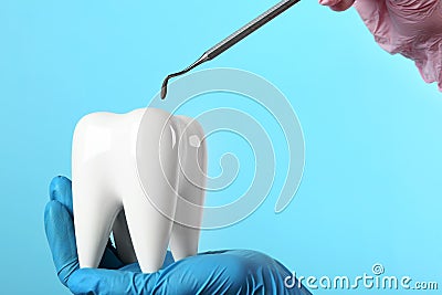 Dentist holding ceramic model of tooth and professional tool on color background Stock Photo