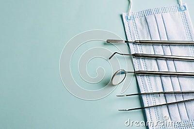 Dentist instruments: mirror and dental probe lying left on medical mask on light blue background. Pattern for advertising Stock Photo