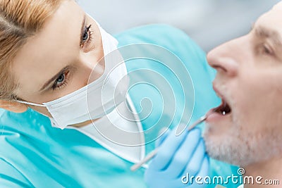 Dentist in medical mask curing mature patient in clinic Stock Photo