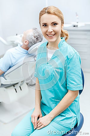 Dentist in medical uniform sitting in clinic and smiling at camera Stock Photo