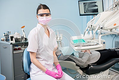 Dentist with patient in the dental office. Doctor wearing glasses, mask, white uniform and pink gloves Stock Photo