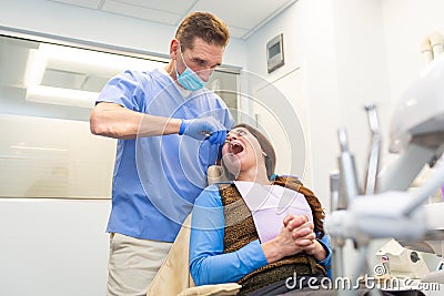 Dentist performing teeth treatment with scared female patient Stock Photo