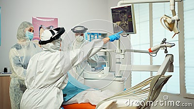 Dentist in ppe suit pointing on digital dental monitor explaining x-ray to mother Stock Photo