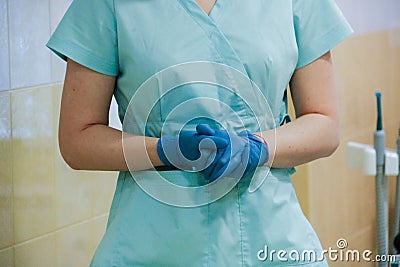 Dentist`s office. The dentist`s gloved hands are folded and the doctor is standing in a special blue medical uniform. Equipment Stock Photo