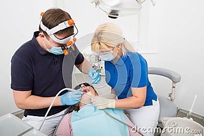 Dentist in scrubs googles and mask at work. female patient visiting dentist office. dentist and assistant. process of dentistry Stock Photo