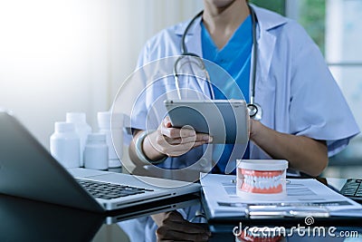 Dentist sitting at table with jaw samples tooth model and working with tablet and laptop in dental office professional dental Stock Photo