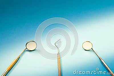 Dentist tools: two mirrors, dental probe and tweezers lying on blue background in light ray Stock Photo