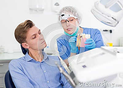 Dentist in uniform with maket of jaw is telling about healthcare in dental clinic Stock Photo