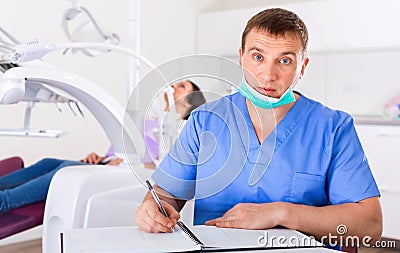 dentist in uniform writing document with visitor in dentist's office Stock Photo