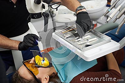 Dentist uses dental curing light for fixing patient`s teeth and takes another dental instrument from a tray Stock Photo