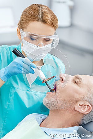 Dentist using dental curing UV lamp on teeth of mature patient Stock Photo
