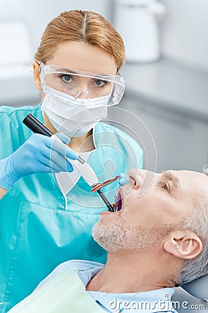 Dentist using dental curing UV lamp on teeth of mature patient Stock Photo