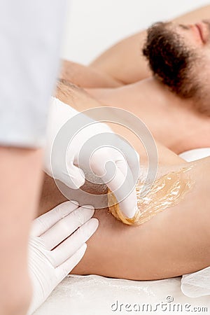 Cosmetologist applying wax paste on male armpit Stock Photo