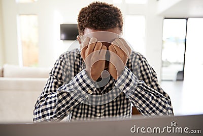 Depressed African American teenage boy with head in hands using a laptop computer at home, front view, close up Stock Photo