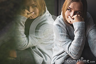 Depressed/anxious young woman sitting by a large window Stock Photo