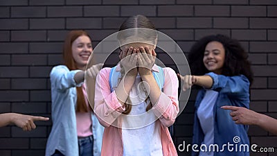 Depressed bullying victim covering face with hands, classmates pointing fingers Stock Photo