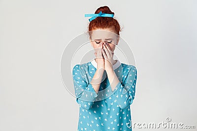 Depressed and crying young caucasian girl with ginger hair feeling ashamed or sick, covering face with both hands Stock Photo