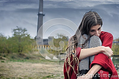 Depressed girl in a red poncho sitting on a bench alone Stock Photo