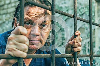 A depressed man in handcuffs behind bars. A depressed arrested male offender is jailed. Shouts, breaks, cries Stock Photo