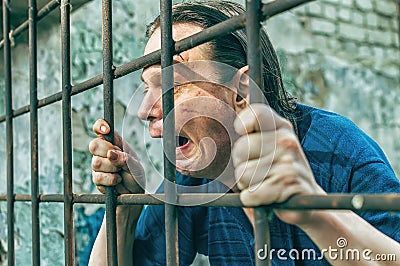 A depressed man in handcuffs behind bars. A depressed arrested male offender is jailed. Shouts, breaks, cries Stock Photo