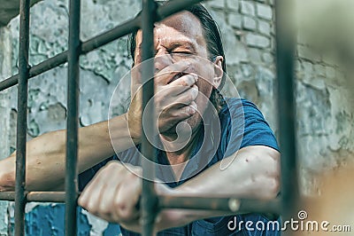 A depressed man in handcuffs behind bars. A depressed arrested male offender is jailed. Shouts, breaks, cries Stock Photo