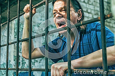 A depressed man in handcuffs behind bars. A depressed arrested male offender is jailed. Shouts, breaks, cries Stock Photo
