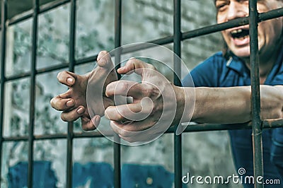 A depressed man holds his hands on the prison bars. Prisoner for the crime. Poor conditions. Stock Photo