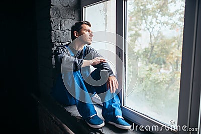 Depressed man sitting on the window sill, psycho Stock Photo