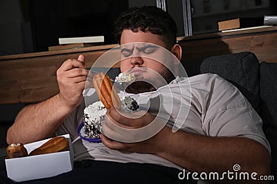 Depressed overweight man eating sweets in room at night Stock Photo