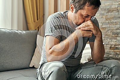Depressed sulking man sitting alone at living room sofa and thinking Stock Photo