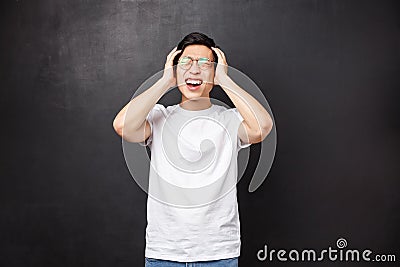 Depressed and tensed young asian guy fed up with studying, have lots on mind, grab head grimacing from pain feel Stock Photo